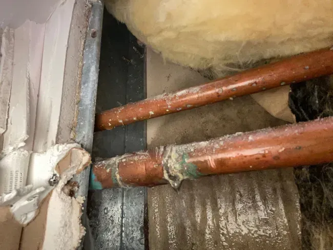 Corroded copper water pipes exposed inside an opened wall, a common source of hidden leaks