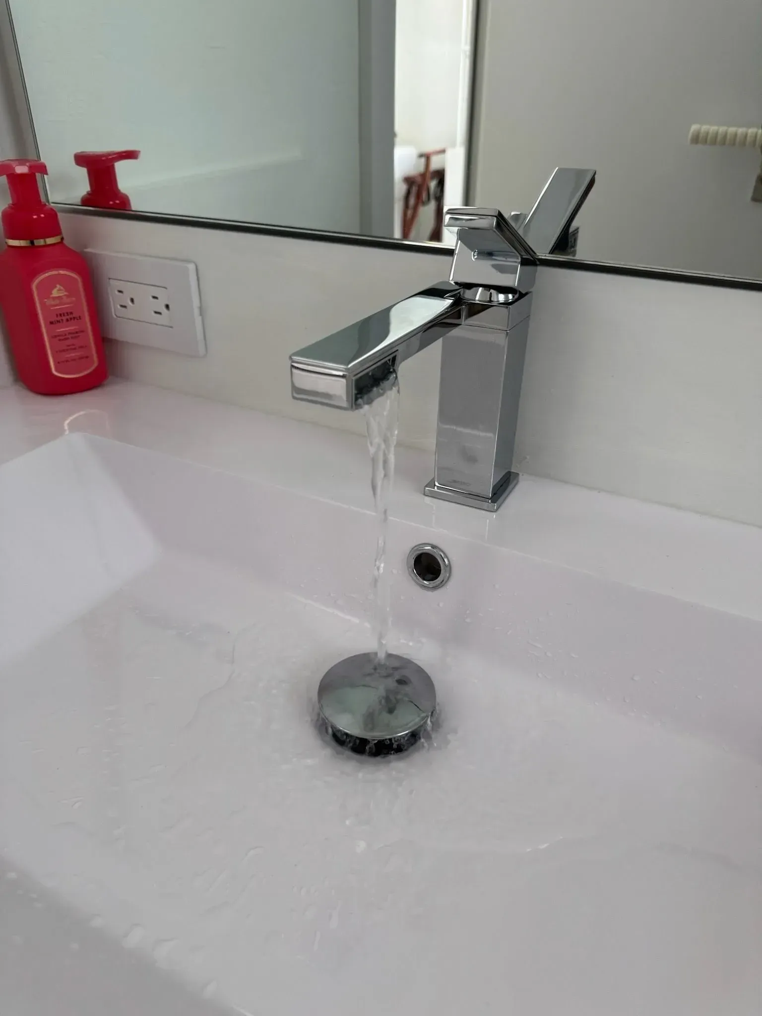 New chrome single-handle faucet running water into a modern white bathroom sink